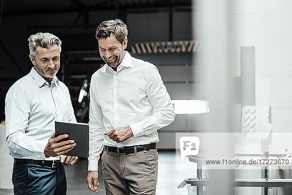 Smiling businessmen discussing over digital tablet while standing in industry