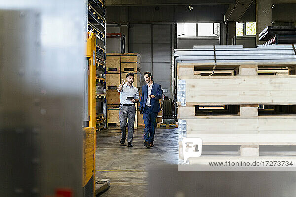 Businessman and colleague inspecting warehouse while walking at factory