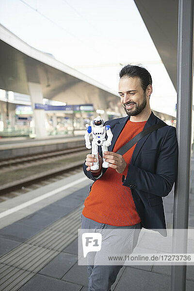 Lächelnder Geschäftsmann  der einen Roboter betrachtet  während er auf einem Bahnsteig steht