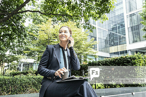 Lächelnde Geschäftsfrau  die ein Mobiltelefon benutzt  während sie im Büropark sitzt