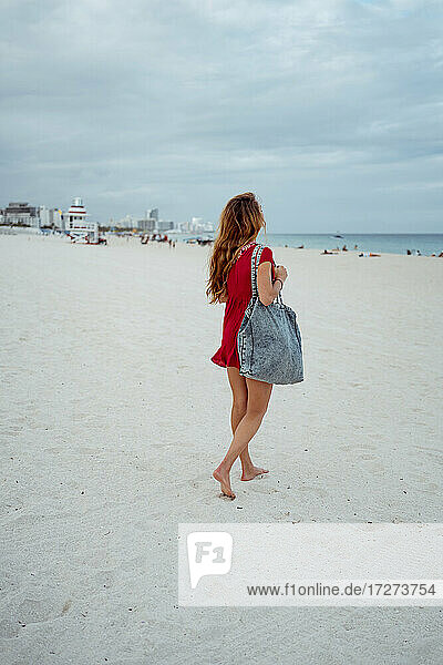 Junge Frau schaut auf das Meer  während sie auf dem Sand gegen den Himmel läuft