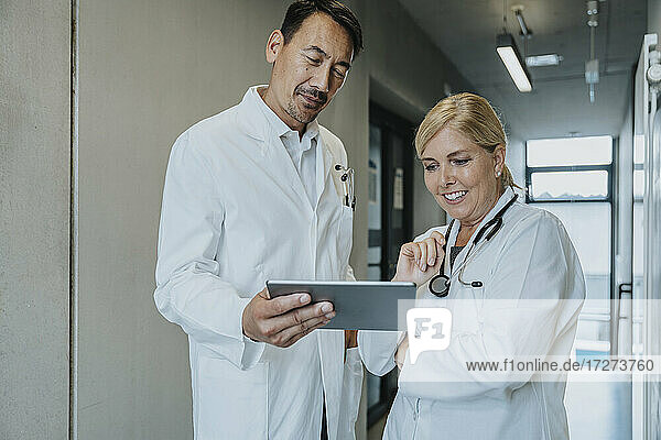 Smiling scientist and doctor using digital tablet while standing at clinic corridor