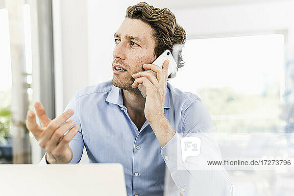 Mid adult man talking on smart phone looking away while sitting in office