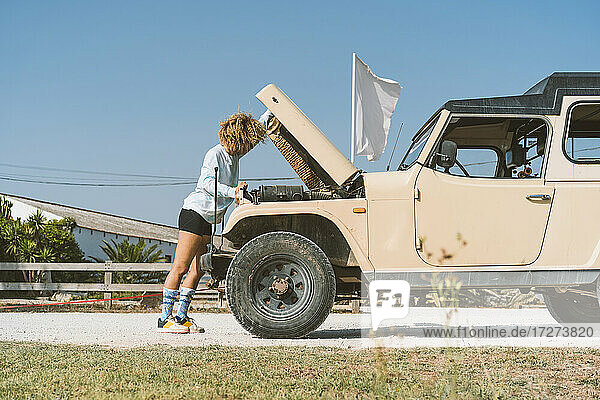 Junge Frau untersucht einen Geländewagen  während sie an einem sonnigen Tag mit offenem Verdeck steht