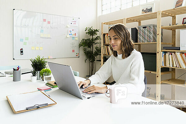 Businesswoman working on laptop while sitting by table at office