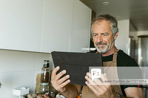 Mann benutzt digitales Tablet  während er zu Hause in der Küche steht