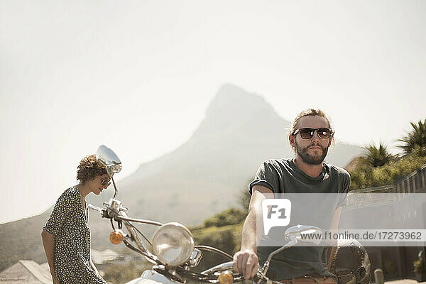 Mittlerer erwachsener Mann auf Motorrad sitzend mit Freundin an einem sonnigen Tag