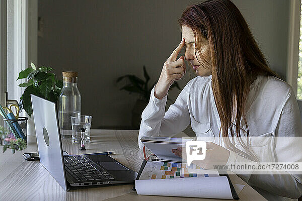 Doctor with headache holding book while working at home