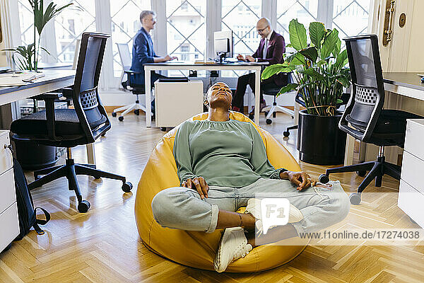 Tired businesswoman with eyes closed resting on bean bag in office