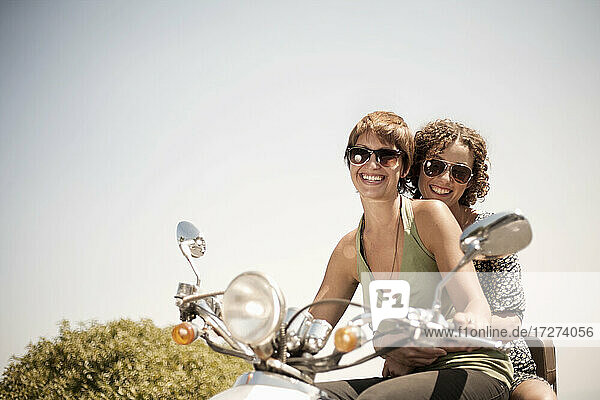 Weibliche Freunde fahren auf dem Motorrad an einem sonnigen Tag