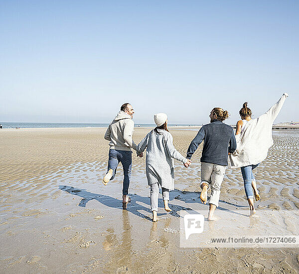 Playful family holding hands while running at beach