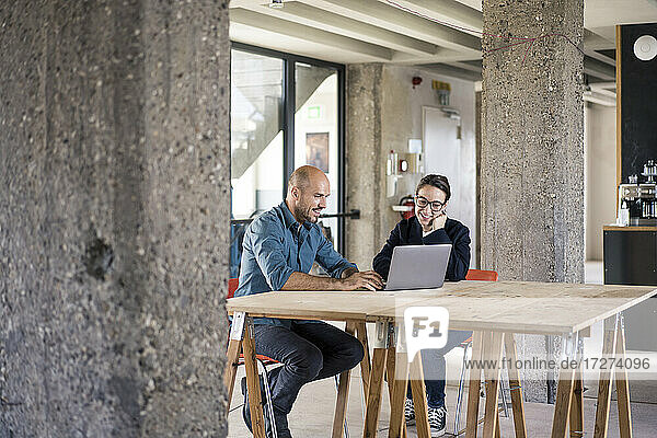 Geschäftsleute arbeiten am Laptop  während sie am Tisch im Büro sitzen