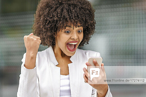 Surprised businesswoman using mobile phone outdoors
