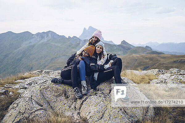 Freunde  die sich umarmen  während sie auf einem Felsen um die Ibones von Anayet sitzen