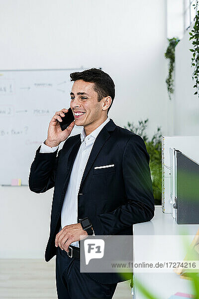 Lächelnder Geschäftsmann  der am Telefon spricht  während er an einem Schrank im Kreativbüro steht