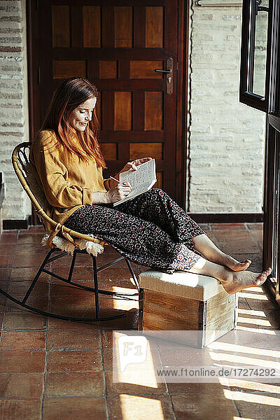 Frau schreibt in ein Buch  während sie zu Hause auf einem Stuhl sitzt