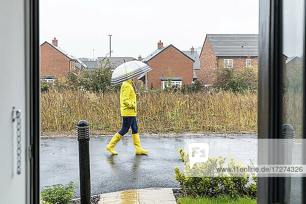 Mittlere erwachsene Frau mit Händen in den Taschen  die einen Regenschirm hält und auf der Straße wacht  während es regnet