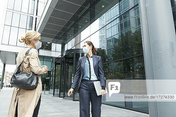 Women wearing face mask talking while standing against office building