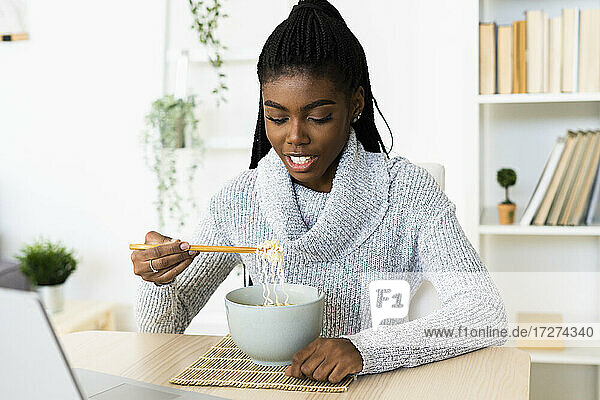 Junge Frau isst Nudeln  während sie zu Hause sitzt