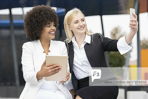 Businesswoman taking selfie through mobile phone while sitting with colleague outdoors