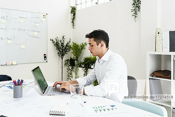 Gut aussehender Geschäftsmann  der einen Laptop benutzt  während er am Schreibtisch eine Strategie für einen kreativen Arbeitsplatz plant