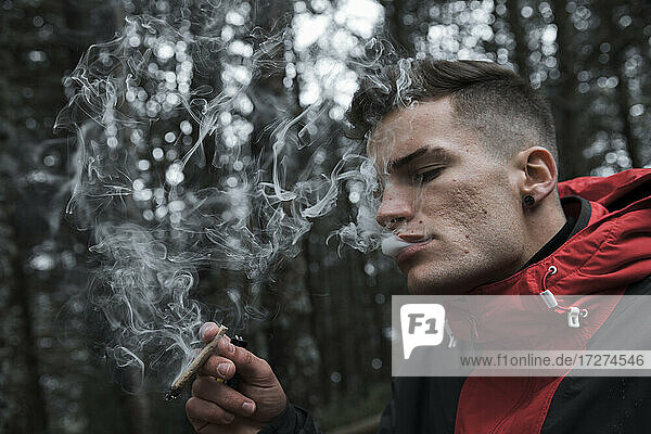 Junger Mann  der im Herbst im Wald steht und eine Zigarette raucht