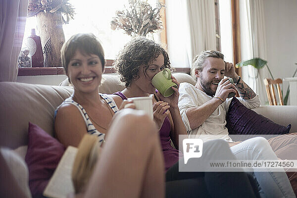 Male and female friends drinking coffee while sitting on sofa at home