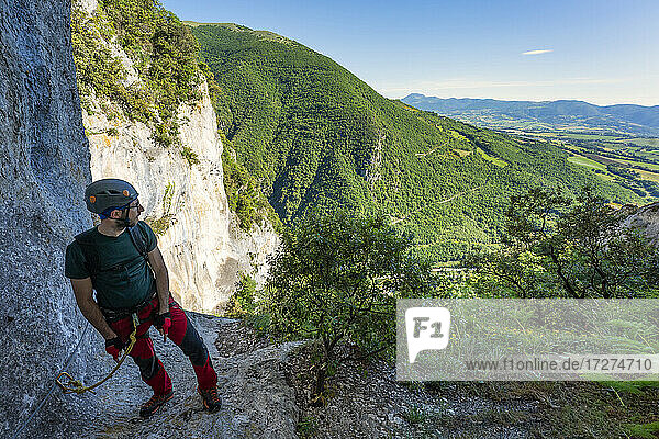 Male rock climber taking break to admire surrounding landscape of Apennine Mountains