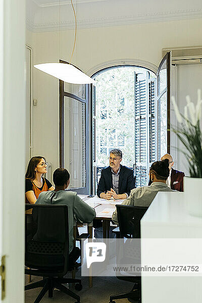 Geschäftsleute und Geschäftsfrauen diskutieren am Tisch in einem Büro  gesehen durch eine Türöffnung