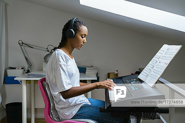 Teenager-Mädchen spielt Klavier  während sie zu Hause sitzt