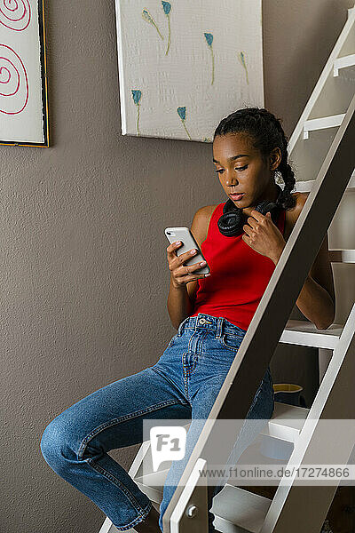 Teenager-Mädchen benutzt ihr Smartphone  während sie zu Hause auf der Leiter sitzt