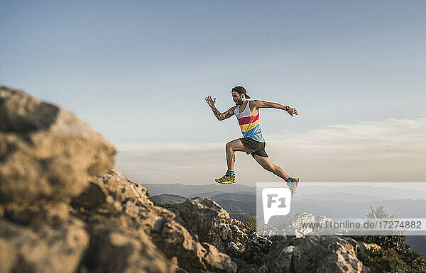 Athlete running on mountain against clear sky during sunset