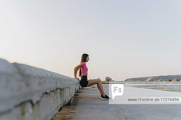 Woman exercising while leaning on wall against clear sky
