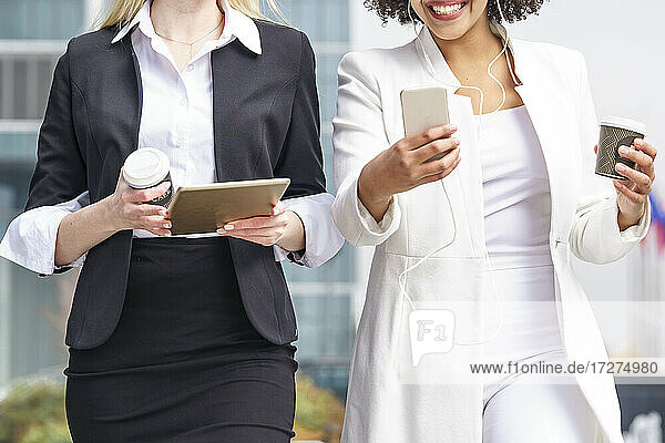 Geschäftsfrauen  die bei einem Spaziergang im Freien ein Mobiltelefon und ein digitales Tablet benutzen