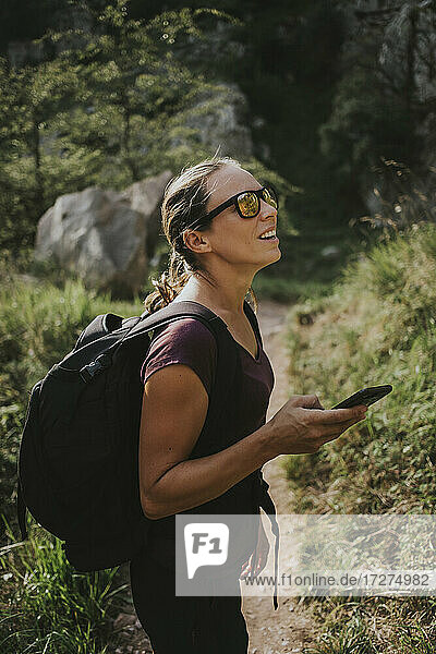 Frau schaut weg  während sie ihr Smartphone zur Navigation beim Wandern an einem sonnigen Tag hält