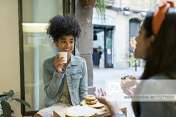 Weibliche Freunde unterhalten sich bei Essen und Trinken am Fenster eines Cafés