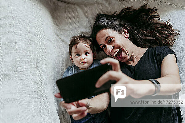 Mutter und Sohn machen ein Selfie mit dem Smartphone  während sie zu Hause im Schlafzimmer liegen