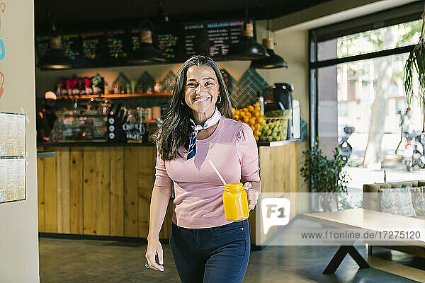 Glückliche Frau hält Einmachglas mit frischem Saft beim Spaziergang im Café