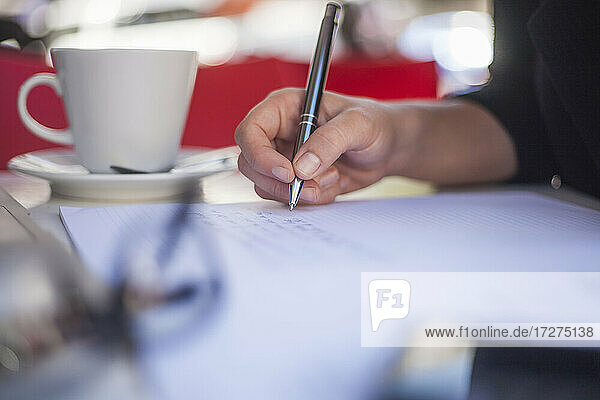 Junge Frau mit Kaffeetasse schreibt in Papier  während sie in einem Straßencafé sitzt