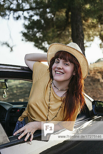 Lächelnde junge schöne rothaarige Frau  die sich aus dem Autofenster lehnt