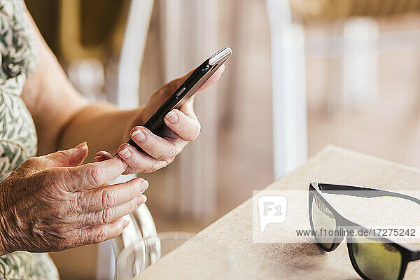 Ältere Frau  die ein Mobiltelefon benutzt  während sie am Tisch eines Cafés sitzt