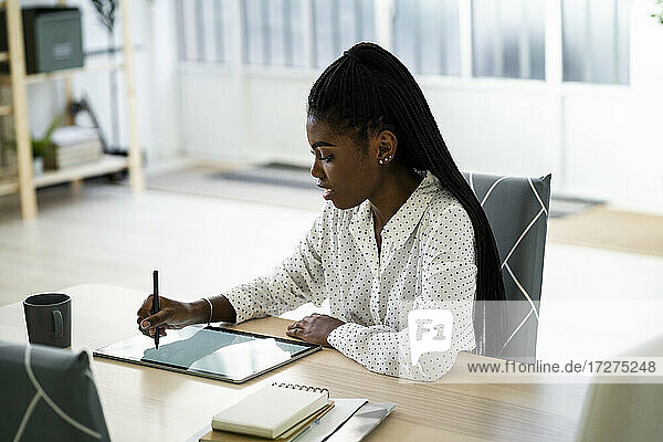 Frau schreibt auf digitalem Tablet  während sie zu Hause im Wohnzimmer sitzt