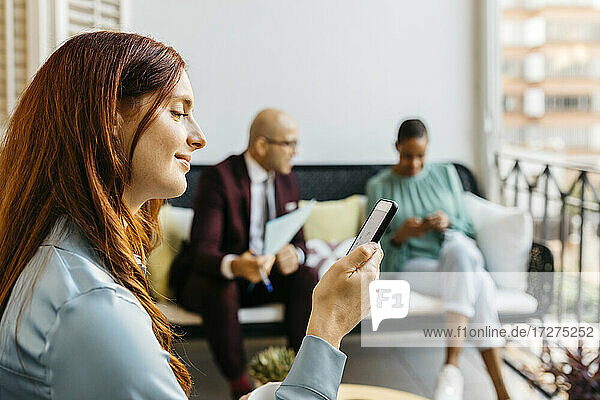 Smiling businesswoman using smart phone while coworkers sitting in balcony