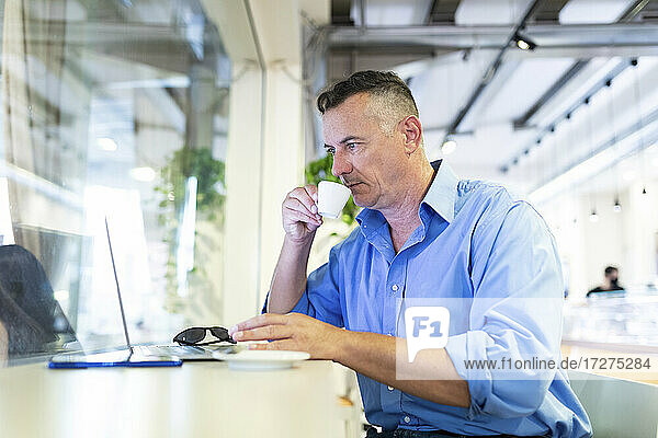 Männlicher Unternehmer trinkt Kaffee und schaut in einem Café auf seinen Laptop