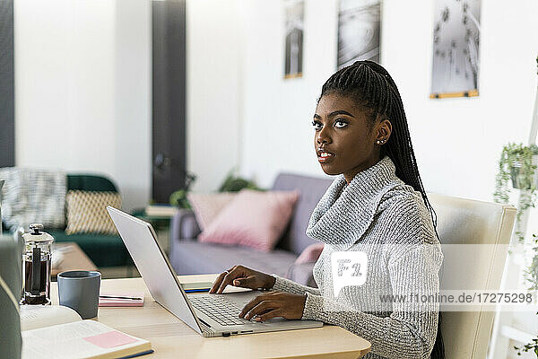 Junge Frau  die wegschaut  während sie zu Hause am Laptop sitzt und studiert