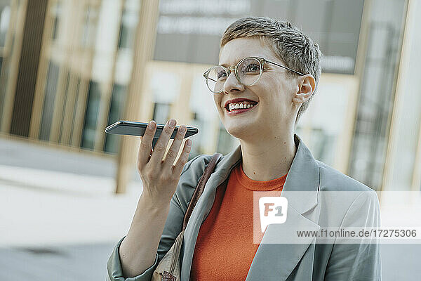 Frau  die eine Sprachnachricht mit ihrem Smartphone sendet  während sie an einem sonnigen Tag auf einer Straße in der Stadt steht