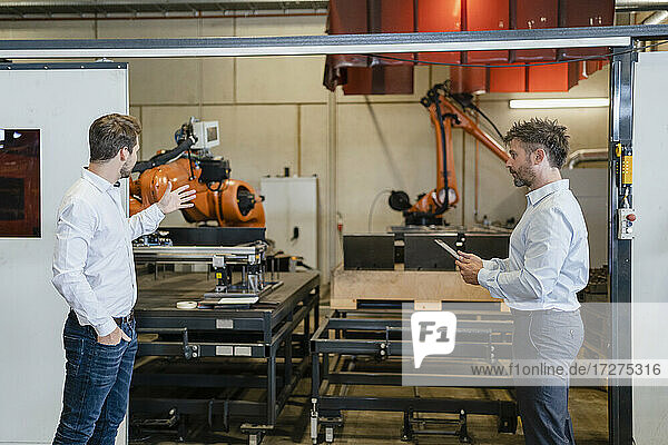 Businessman having discussion with colleague while standing by robotic arm machine at factory
