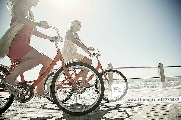 Junge Freundinnen  die an einem sonnigen Tag auf der Promenade am Strand Rad fahren
