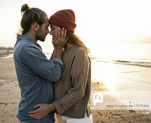 Romantischer junger Mann steht von Angesicht zu Angesicht mit seiner Freundin am Strand bei Sonnenuntergang