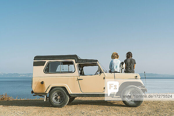 Junger Mann und Frau bewundern die Aussicht auf das Meer  während sie mit ihrem Hund im Auto am Strand sitzen